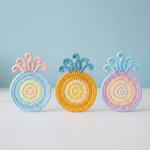 Può includere: Tre sottobicchieri a forma di ananas all'uncinetto fatti a mano in colori pastello. Ogni sottobicchiere presenta un design circolare con anelli concentrici di colore, tra cui blu, giallo e rosa. Le cime hanno un design riccio a forma di fronda.