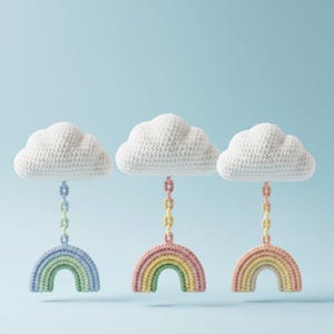 Puede incluir: Tres móviles de arcoíris de ganchillo con nubes blancas y coloridos arcosíris. Cada arcoíris está suspendido por una cadena. El fondo es azul claro.