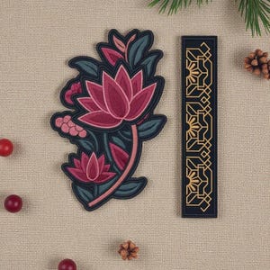 May include: A decorative patch featuring a stylized pink lotus flower with green leaves and a black border. Next to it is a black rectangular patch with a gold geometric design. The patches are on a beige textured surface.