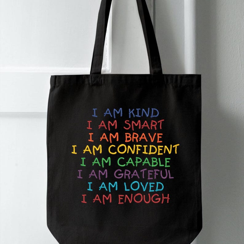 May include: Black tote bag with the text "I am kind, I am smart, I am brave, I am confident, I am capable, I am grateful, I am loved, I am enough" in rainbow colors.