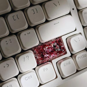 May include: Close-up of a computer keyboard with white keys. The Enter key is replaced with a custom keycap filled with red glitter and silver flakes. Other keys include Ctrl, Alt, Fn, and End.