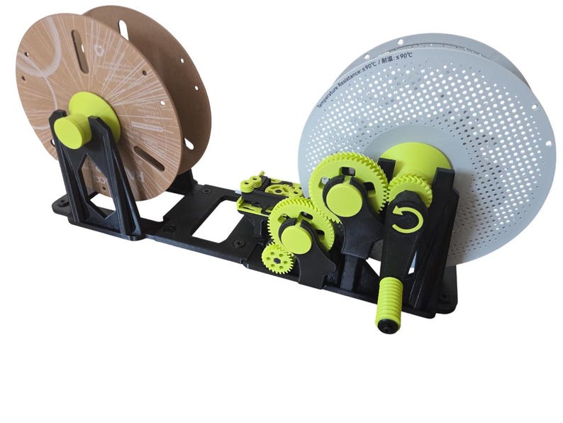 May include: A black and lime green 3D printer filament spool winder featuring a manual hand crank, a series of interlocking gears, and two circular spool holders. One spool is light brown, and the other is white with a perforated surface pattern.