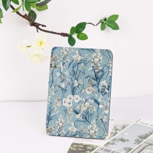 May include: A rectangular, floral-patterned object featuring a blue background with white and gray orchid illustrations. The design includes various orchid species and foliage. The object is positioned upright, showcasing the detailed botanical print.