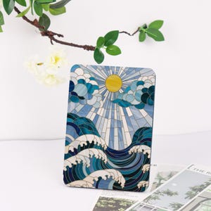 May include: A rectangular decorative panel with a stained glass design. The artwork shows a yellow sun, blue clouds, and ocean waves in shades of blue and white. The panel has a dark border. The design is reminiscent of a seascape.