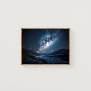 May include: A framed landscape photograph of a night sky filled with stars and the Milky Way galaxy. The image features a river valley with dark mountains in the foreground, under a vibrant, starry sky. The wooden frame adds a natural touch.