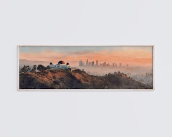Könnte beinhalten: Ein panoramisches gerahmtes Wandbild, das das Griffith-Observatorium auf einem Hügel im Vordergrund zeigt, mit der Skyline von Los Angeles in der Ferne unter einem weichen, dunstigen, orangefarbenen und rosafarbenen Sonnenuntergangshimmel.