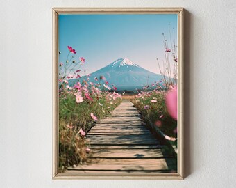 May include: Framed print of a scenic landscape featuring a wooden pathway leading towards a snow-capped mountain under a clear blue sky. Pink flowers bloom on either side of the path. The frame is a light wood color.