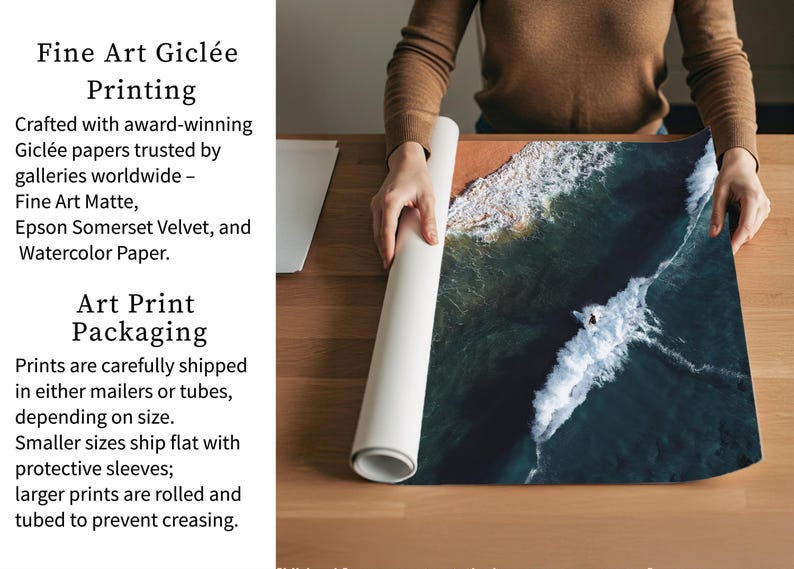 a person carefully handling a roll of paper, possibly for art print packaging. The person is standing behind a wooden table, which has a large piece of paper on it. The paper appears to be a watercolor print of a seascape, with waves crashing against the shore. The person is holding the paper up to the light, possibly to examine it or prepare it for printing.