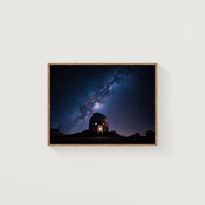 May include: A framed print of an observatory under a starry night sky. The observatory is silhouetted against the dark sky, with a bright light emanating from its windows. The Milky Way galaxy is visible above.
