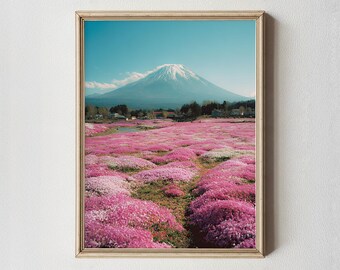 May include: A framed print of a scenic landscape featuring a snow-capped mountain under a clear blue sky. The foreground is filled with a field of vibrant pink flowers, creating a picturesque view. The frame is a light wood color.