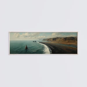 Op de afbeelding: Een panoramisch landschapsschilderij in een lichthouten lijst met een donker vulkanisch zandstrand dat de turquoise oceaan ontmoet. Grillige rotsformaties steken uit het water bij een verre klif onder een lucht vol zachte witte wolken.