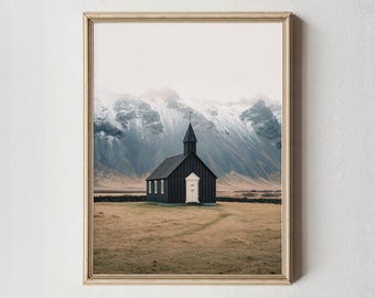 Pode incluir: Impressão emoldurada com uma igreja preta com uma porta e janelas brancas, contra um fundo de montanhas cobertas de neve e um campo de grama seca. A igreja tem uma torre e é emoldurada em uma moldura de madeira clara.