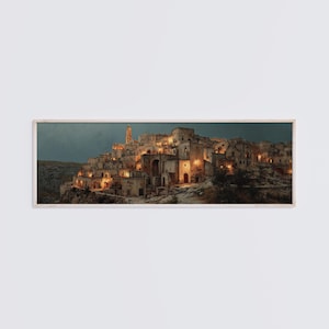 May include: A panoramic framed wall art print depicting a historic stone city built into a cliffside at twilight. The scene features warm golden lights illuminating the ancient buildings and a tall bell tower against a dark blue evening sky.