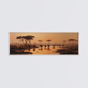 May include: A panoramic framed wall art print depicting a herd of elephants gathered at a watering hole during a golden sunset. The scene features silhouettes of acacia trees against a warm orange sky, with the animals reflected in the water.