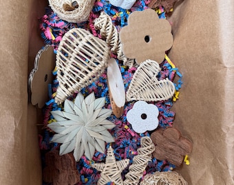 May include: A box filled with a variety of natural and woven pet toys, including hearts, stars, flowers, and a loofah. The toys are in a brown paper bag with colorful shredded paper.