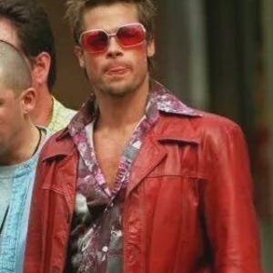 Peut inclure: Veste en cuir rouge avec deux poches avant et une chemise à motifs. La personne porte des lunettes de soleil rouges. La veste est d'un rouge vif, un style classique.