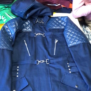 Könnte beinhalten: Marineblaue Jacke mit passender Kapuze. Die Jacke hat gesteppte Schulterpartien, silberne Reißverschlüsse und dekorative Schnallen. Sie hat eine taillierte Passform mit Taschen und einem Gürteldetail und bietet einen stilvollen, strukturierten Look.