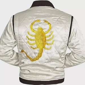 May include: White satin jacket with a quilted pattern and a large gold scorpion embroidered on the back. The jacket has a black collar and trim, and long sleeves. A stylish outerwear piece.