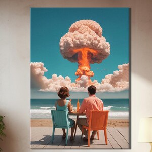 May include: A framed art print depicts a couple seated at a table on a beach, with a nuclear explosion in the background. The couple is seated in blue and orange chairs. The sky is blue with white clouds. The print is displayed in a modern interior.