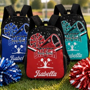 May include: Three backpacks featuring a cheerleading theme with black straps and accents. Each bag displays a glittery megaphone, pom-poms, a silhouette of a cheerleader, the word "CHEER," "Team Name," and the name "Isabella" in white script.
