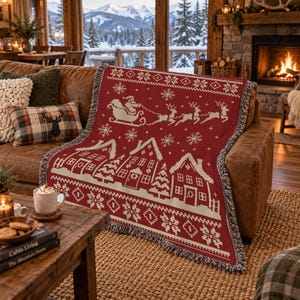 May include: A red and cream woven throw blanket featuring a repeating pattern of Santa Claus in a sleigh pulled by reindeer, snowflakes, and a row of houses. The blanket has a fringed edge and a detailed, pixelated-style winter holiday design.