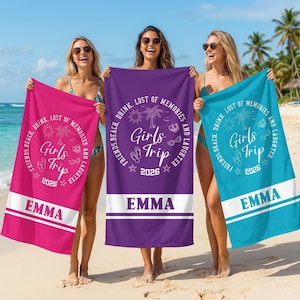 Könnte beinhalten: Drei Frauen halten personalisierte Strandtücher. Die Tücher sind in Pink, Lila und Türkis gehalten und tragen den Text "Girls Trip 2026" und den Namen "EMMA". Die Tücher haben auch ein kreisförmiges Design mit Palmen und Strandmotiven.