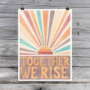 May include: A watercolour print featuring a colourful sunburst design and the text "Together We Rise" in a brown and orange font.