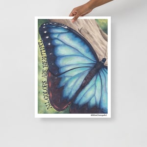 Puede incluir: Un póster con una pintura de acuarela de una mariposa azul con detalles en negro. La obra de arte incluye el texto "ALL COLORS ARE BEAUTIFUL" en orientación vertical. La mariposa se encuentra sobre un fondo marrón claro.