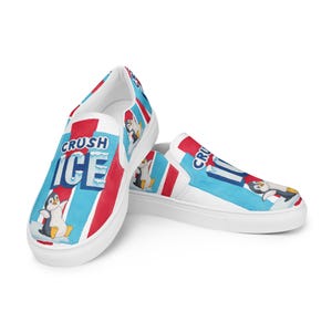 May include: White slip-on shoes with a colorful design featuring the words "CRUSH ICE" in blue and red, along with cartoon penguins. The shoes have a white sole and a blue and red striped pattern.