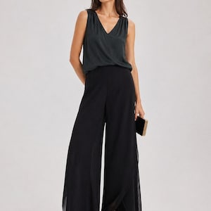 May include: A woman wearing a dark green sleeveless top with a V-neck and black wide-leg pants. She is holding a small black clutch and wearing black sandals. The outfit is suitable for formal occasions.