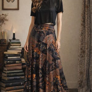 Peut inclure: Un haut noir à manches courtes associé à une longue jupe à motifs. La jupe présente un motif patchwork avec des nuances de marron, d'orange et de noir. La tenue est présentée dans une pièce avec une pile de livres et une impression de papillon encadrée.