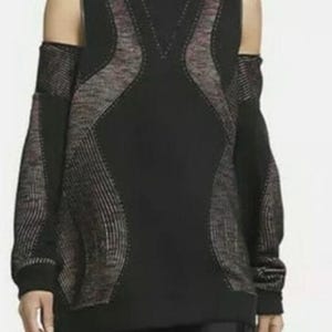 May include: Black long-sleeved top with a high neck and cut-out shoulders. The top features a textured design in shades of gray and pink, creating a contrasting pattern against the black fabric. The sleeves extend to the wrists.