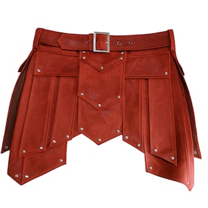 Op de afbeelding: Een rode leren kilt met een riem en gesp. De kilt heeft decoratieve panelen met zilveren klinknagels en een uniek, gelaagd ontwerp. De riem heeft een zilveren gesp en is vastgezet met klinknagels. Een opvallend kledingstuk.