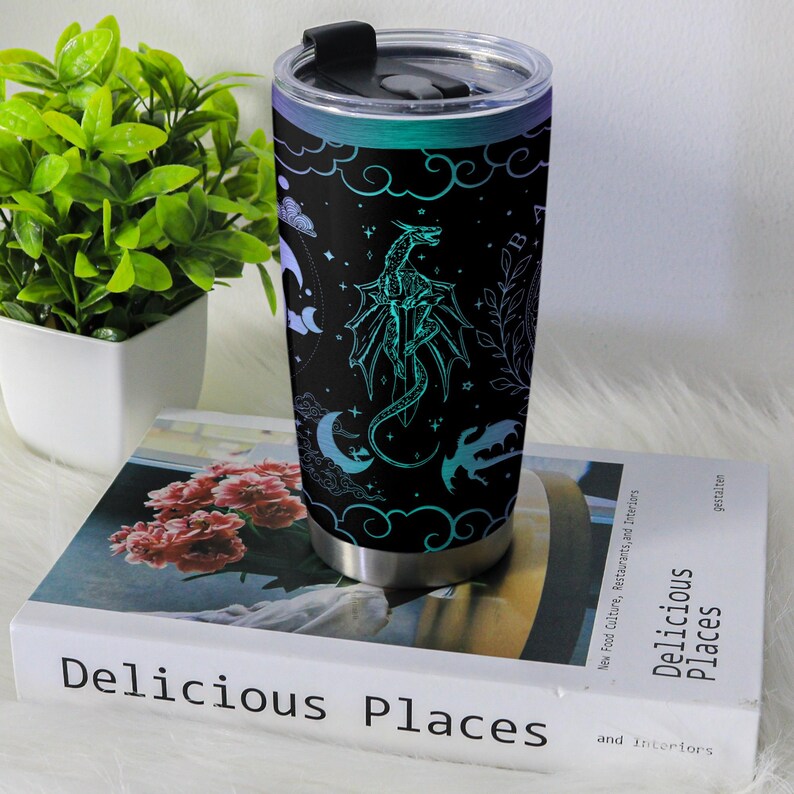 May include: Stainless steel travel mug with a black background and a teal dragon design. The design includes clouds, stars, and crescent moons. The lid is black with a sliding closure.