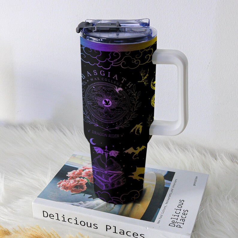 May include: Black travel mug with a white handle, featuring a design with dragons, a sword, and the text "BASGIATH WAR COLLEGE DRAGON RIDER". The mug has a gradient of purple, yellow, and blue colors.