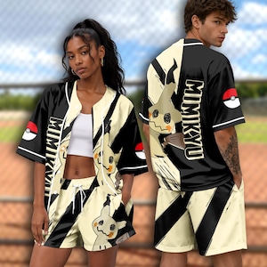 May include: A black and cream baseball jersey and shorts set featuring a Mimikyu character graphic, the text "MIMIKYU" in bold lettering, and red and white Poké Ball icons on the sleeves. The garments have a button-down front and drawstring waist.