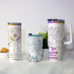 May include: Three white insulated tumblers with fantasy-themed designs. One features a dragon and the text "DRAGON RIDERS". Another has a map design, and the third has the text "IRON FLAME" and "violence". Each tumbler has a different lid and handle.