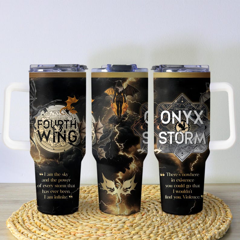 May include: Three black insulated tumblers with white handles and lids. Each tumbler features a different design with gold accents and text. The text includes "FOURTH WING" and "ONYX STORM" with quotes. The tumblers are on a woven mat.
