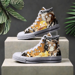 Könnte beinhalten: High-Top-Sneaker mit weißer Gummikappe und Sohle mit schwarzem Streifen. Das Obermaterial aus Canvas zeigt eine gelbe und braune Charaktergrafik mit japanischem Text vor einem schwarz-orangen abstrakten Hintergrund mit weißen Schnürsenkeln.