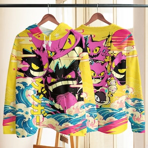 Puede incluir: Una sudadera con capucha amarilla y una sudadera de cuello redondo amarilla con un estampado vibrante de personajes Gengar morados, olas oceánicas azules y texto japonés. El diseño incluye múltiples ilustraciones de la criatura con ojos amarillos y dientes afilados, sobre un fondo amarillo brillante con acentos gráficos en rosa y azul.