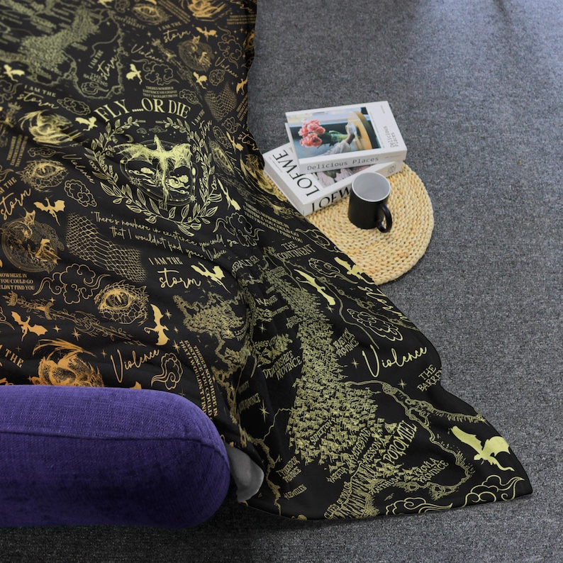 May include: Black and gold patterned blanket with text and illustrations. The blanket features phrases like "FLY OR DIE" and "I AM THE STORM", along with a map design and other graphics. A purple pillow is visible.