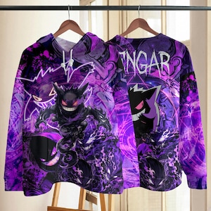 Puede incluir: Una sudadera con capucha morada que presenta un estampado gráfico del personaje Gengar. El diseño incluye patrones de energía morados en espiral, una gran ilustración de Gengar y el texto GENGAR impreso en una fuente blanca estilizada a la derecha.