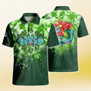 Puede incluir: Un polo verde con patrón tie-dye, que presenta una serie de rostros de criaturas estilizadas en el frente y una gran ilustración de una criatura con una flor roja en la espalda en la parte posterior. El diseño incluye motivos de hojas y un logo.