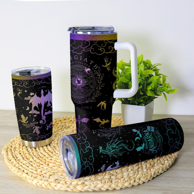 May include: A collection of black insulated tumblers with dragon-themed designs. The tumblers feature illustrations of dragons, clouds, and celestial elements in purple, gold, and teal. One tumbler has a white handle. The text on the tumblers reads "Save a Dragon" and "Andarna".