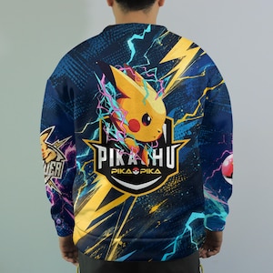 May include: A long-sleeve sweatshirt featuring a vibrant graphic of the yellow character Pikachu surrounded by blue and yellow lightning bolts. The design includes the text PIKACHU and PIKA PIKA with a Pok&eacute; Ball icon on a dark blue background.