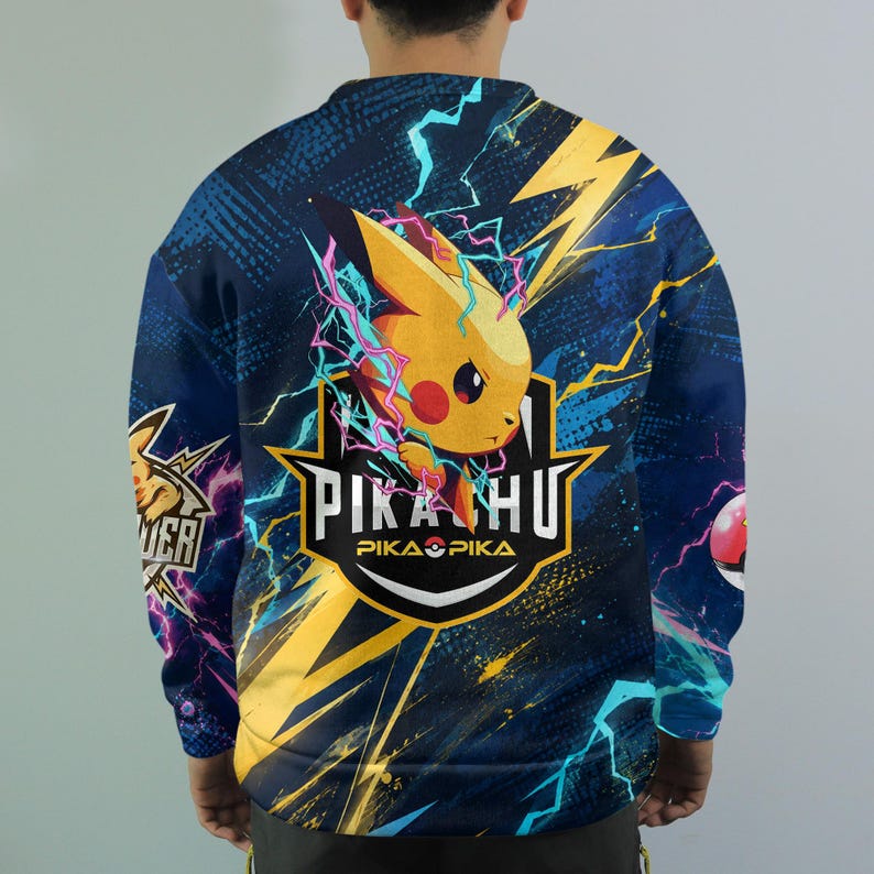 May include: A long-sleeve sweatshirt featuring a vibrant graphic of the yellow character Pikachu surrounded by blue and yellow lightning bolts. The design includes the text PIKACHU and PIKA PIKA with a Pok&eacute; Ball icon on a dark blue background.