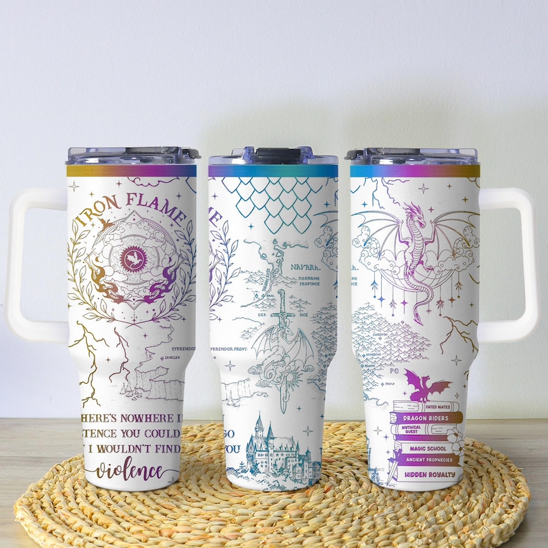 May include: Three white travel mugs with colorful lids and handles. Each mug features a different fantasy-themed design with text. One mug has a dragon and the words "Dragon Riders". The mugs are on a woven mat.