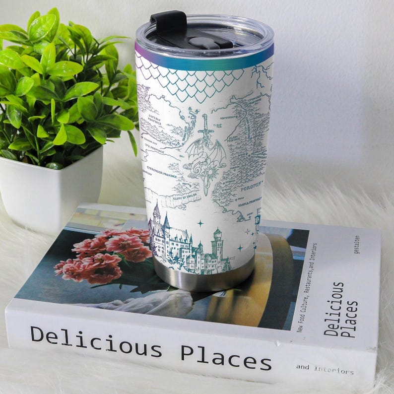 May include: A stainless steel travel mug with a black lid and a white background. The mug features a teal and blue map design with castles, a sword, and a dragon. The top rim has a rainbow gradient.