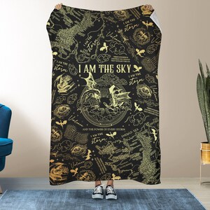 May include: Black blanket with a gold map and dragon design. The text "I AM THE SKY" is prominently displayed, along with other phrases like "I AM THE storm" and "Violence". The blanket is held up by a person.