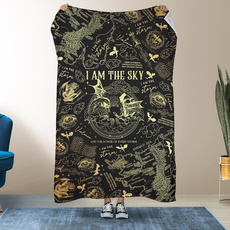 May include: Black blanket with a gold map and dragon design. The text "I AM THE SKY" is prominently displayed, along with other phrases like "I AM THE storm" and "Violence". The blanket is held up by a person.